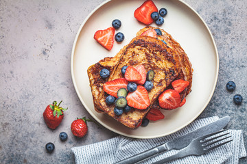 Traditional french toasts with blueberries and strawberries on white plate, top view.