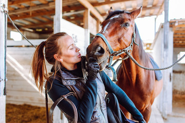Portrait beautiful smiling woman long hair next to her horse in a stable. Horseback riding