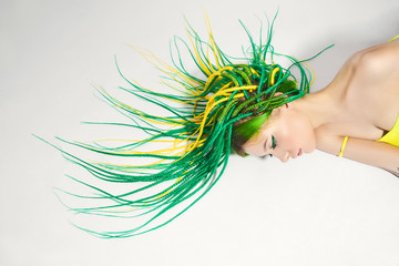 Portrait of a woman with creatively colored hair in green and yellow color. Colorful bright dreadlocks, beautiful modern makeup