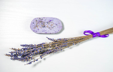 Horizontal photo. Dried lavender flowers lie next to handmade lavender soap on a white background with a wooden texture. Top view. The concept of accessories for personal care and spa.