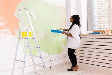 Lovely african american housewife painting wall. Renovation, redecoration and repair concept.