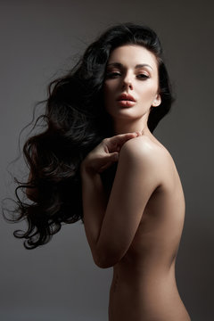 Sexy fashion nude woman with long hair, curly strong hair of a brunette girl. Natural cosmetics for hair care, strong roots