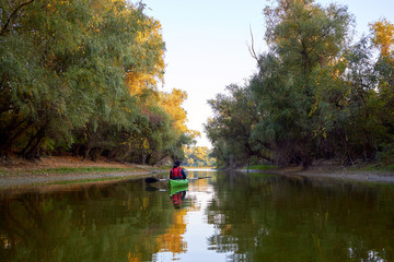 Woman rowing in a green kayak in early autumn along the trees at the bank of Danube river