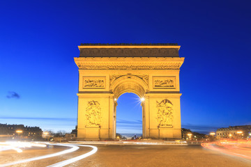 Fototapeta na wymiar Beautiful cityscape urban street view of the Arc de Triomphe in Paris, France, on a spring evening after sunset in the blue hour, seen from the Champs-Elysees with traffic