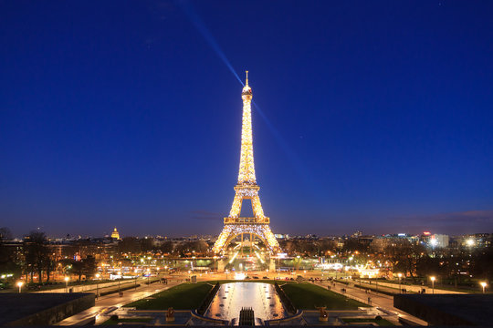 Beautiful cityscape urban street view of the illuminated Eiffel tower in Paris, France, on a spring evening after sunset in the blue hour, seen from Trocadero square
