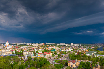 Fototapeta na wymiar Beautiful dark blue thundercloud over the city. Top view of the city. Aerial photography. Houses, streets, green trees and parks. Cars are driving along the avenues.