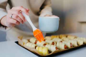 House wife cooking a sausages in the dough. Brush the egg yolk. Quarantine home recepies.