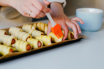 House wife cooking a sausages in the dough. Brush the egg yolk. Quarantine home recepies.