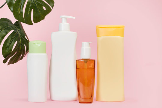 Potes y envases de crema para el cuerpo y la cara junto a hojas monstera sobre un fondo rosa liso y aislado. Vista de frente. Copy space