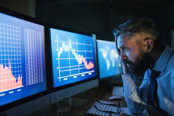 Frustrated businessman with computer sitting at desk, working late. Financial crisis concept.