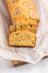 Homemade sliced healthy banana bread ready for serve on breakfast on the white concrete background with craft baking paper and pastry knife. Top view. Close up shoot