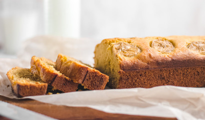 Homemade sliced healthy banana bread ready for serve on breakfast on the white concrete background with craft baking paper and pastry knife, glass of milk. Top view. Close up shoot