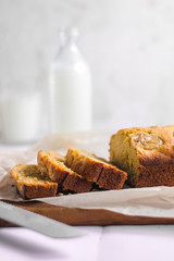 Homemade sliced healthy banana bread ready for serve on breakfast on the white concrete background with craft baking paper and pastry knife, glass of milk. Top view. Close up shoot