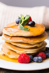 Pile of pancakes with blueberries and raspberries and maple syrup for breakfast on wooden table.