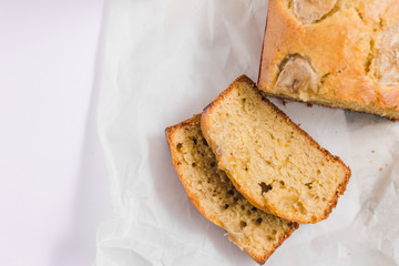 Homemade sliced healthy banana bread ready for serve on breakfast on the white concrete background with craft baking paper and pastry knife. Top view. Close up shoot