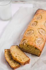 Homemade sliced healthy banana bread ready for serve on breakfast on the white concrete background with craft baking paper and pastry knife, glass of milk. Top view. Close up shoot