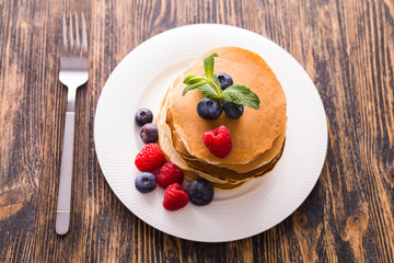 Homemade sweet pancakes with blueberries and raspberries on a white plate, top view.