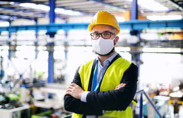 Technician or engineer with protective mask and helmet standing in industrial factory.