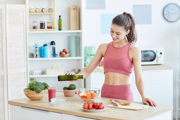 Waist up portrait of fit young woman pouring olive oil into salad while cooking fitness food in kitchen interior, copy space