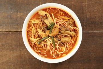 Malaysian curry yellow mee noodle with roasted chicken slice in white bowl on rustic wooden background