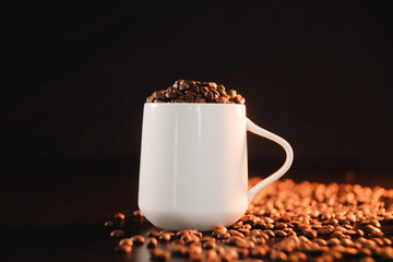 A white coffee cup filled with roasted dark coffee beans.