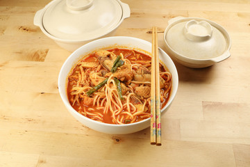 Malaysian curry yellow mee noodle with roasted chicken slice in white bowl chopstick on wooden background