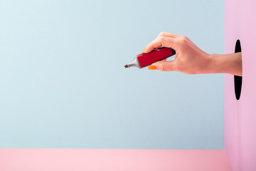 Hand holding a red felt-tip pen marker on blue and pink background
