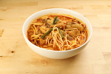 Malaysian curry yellow mee noodle with roasted chicken slice in white bowl on wooden background