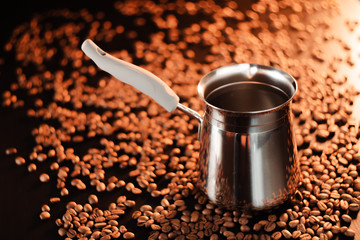 Freshly brewed coffee in cezve on a dark golden background next to scattered roasted coffee beans.