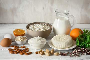 Foods rich in calcium. Dairy products, nuts, beans, eggs, fruits, greens on a white wooden table.