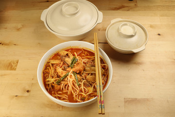 Malaysian curry yellow mee noodle with roasted chicken slice in white bowl on wooden background
