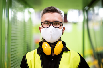 Man worker with protective mask standing in industrial factory or warehouse. - Powered by Adobe