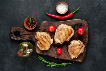 
Skinless grilled chicken thighs with spices on a cutting board on a stone background