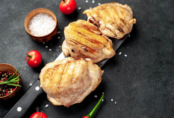 Skinless grilled chicken thighs with spices over a meat knife on a stone background
