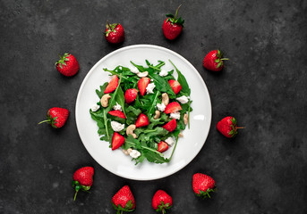 Salad of arugula, nuts, strawberries, cheese in a white plate on a stone background. Healthy food.
