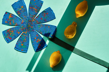 A composite frame with a blue massager shaped like a flower on a green background and lemons, with bands of sun and shade. Top view, flat lay.  For relaxation and health.