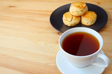 Closeup a cup of hot tea with a plate of scones served on wooden table