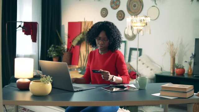 African-American lady is using a laptop and a card to shop from home. Online shopping cocncept.