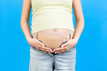 Close up of pregnant woman wearing pregnancy corset against backpain at blue background with copy space. Orthopedic abdominal support belt concept