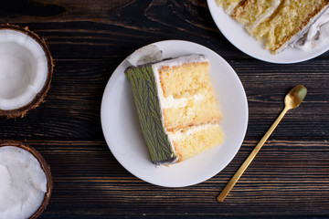 Delicious biscuit cake with coconut impregnation, pineapple slices, cut. Cake on white dishes, on the table. View from above.