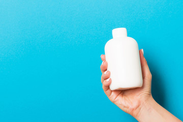 Woman's hand is holding a cosmetics bottle at blue background with copy space for your design
