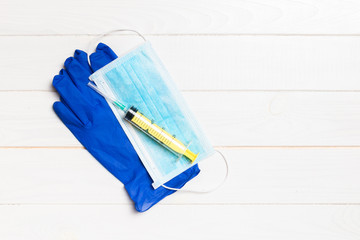 Top view of disposable surgical mask, pair of latex medical gloves and syringe on wooden background. Protect your health concept with copy space