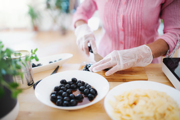 Unrecognizable woman with gloves cooking in kitchen indoors. Hygiene concept.