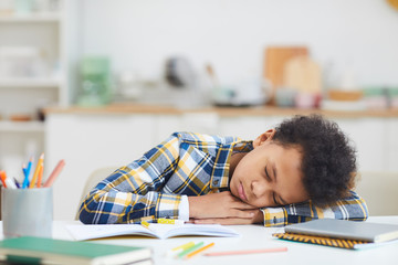 Portrait of exhausted African-American boy sleeping at desk while doing homework, copy space