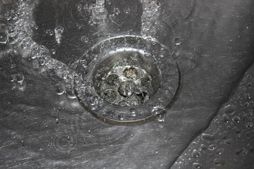 Drain in a metal sink with a stream of water with bubbles.