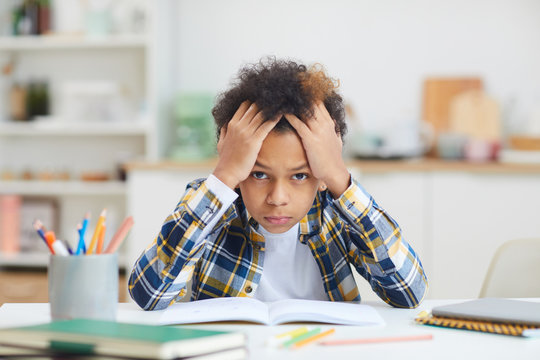 Portrait of cute African-American boy sitting at desk and looking at camera while struggling to finish homework, copy space