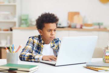 Portrait of teenage African boy using laptop while studying at home, remote education concept, copy space