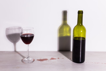 Bottle with wine and glass, red puddle of wine on the table. Cleaning after party concept.