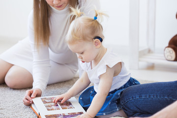 Hearing aid in baby girl's ear. Toddler child wearing a hearing aid at home. Disabled child, disability and deafness concept.