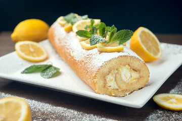 Lemon roll cake decorated with slices of lemon fruit and leaves of mint